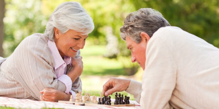 Älteres Paar spielt Schach auf einer Decke im Park.