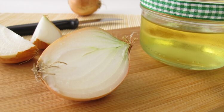 Eine aufgeschnittene Zwiebel neben einem Glas mit Zwiebelsaft