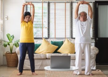 Älteres Paar praktiziert Tai Chi zuhause vor dem Notebook.