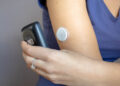 Eine Frau hält ihr Smartphone an ihren Blutzucker-Tracker am Arm.