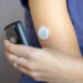 Eine Frau hält ihr Smartphone an ihren Blutzucker-Tracker am Arm.
