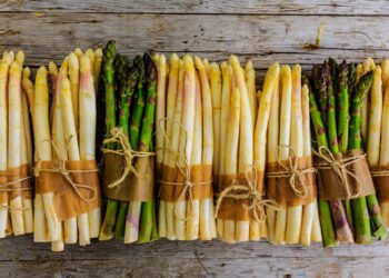 Einige Bündel von grünem und weißem Spargel liegen auf einer Holzoberfläche.