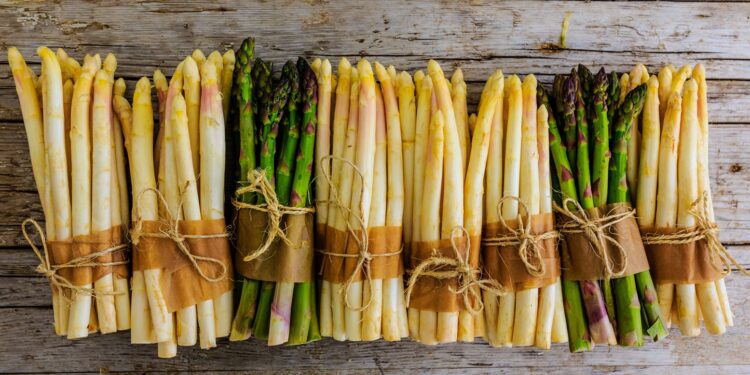 Einige Bündel von grünem und weißem Spargel liegen auf einer Holzoberfläche.