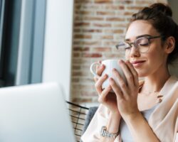 Frau sitzt auf dem Sofa und hält mit beiden Händen eine Tasse Kaffee.