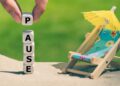 Liegestuhl am Strand mit Schirmchen und das Wort Pause aus Buchstabenwürfeln