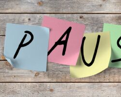 Das Wort Pause in einzelnen Großbuchstaben auf bunten Post-its geschrieben, die an einer Holzwand kleben