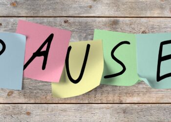 Das Wort Pause in einzelnen Großbuchstaben auf bunten Post-its geschrieben, die an einer Holzwand kleben