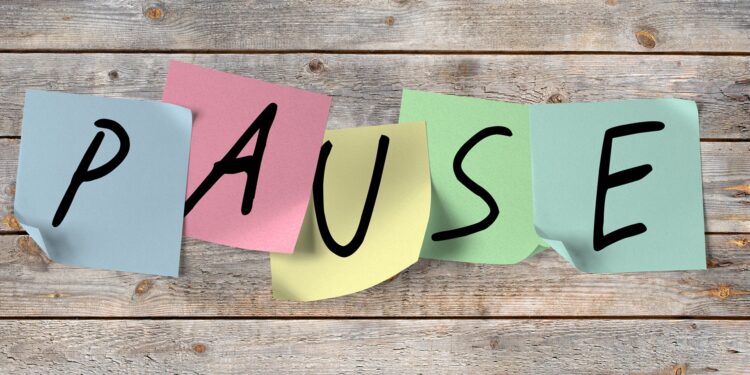 Das Wort Pause in einzelnen Großbuchstaben auf bunten Post-its geschrieben, die an einer Holzwand kleben