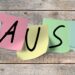 Das Wort Pause in einzelnen Großbuchstaben auf bunten Post-its geschrieben, die an einer Holzwand kleben