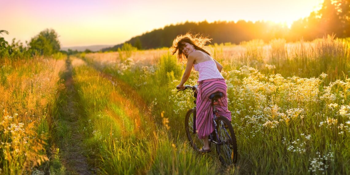 Frau fährt mit dem Rad durch sommerliches Feld
