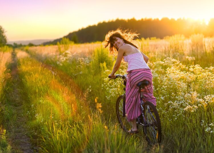 Frau fährt mit dem Rad durch sommerliches Feld